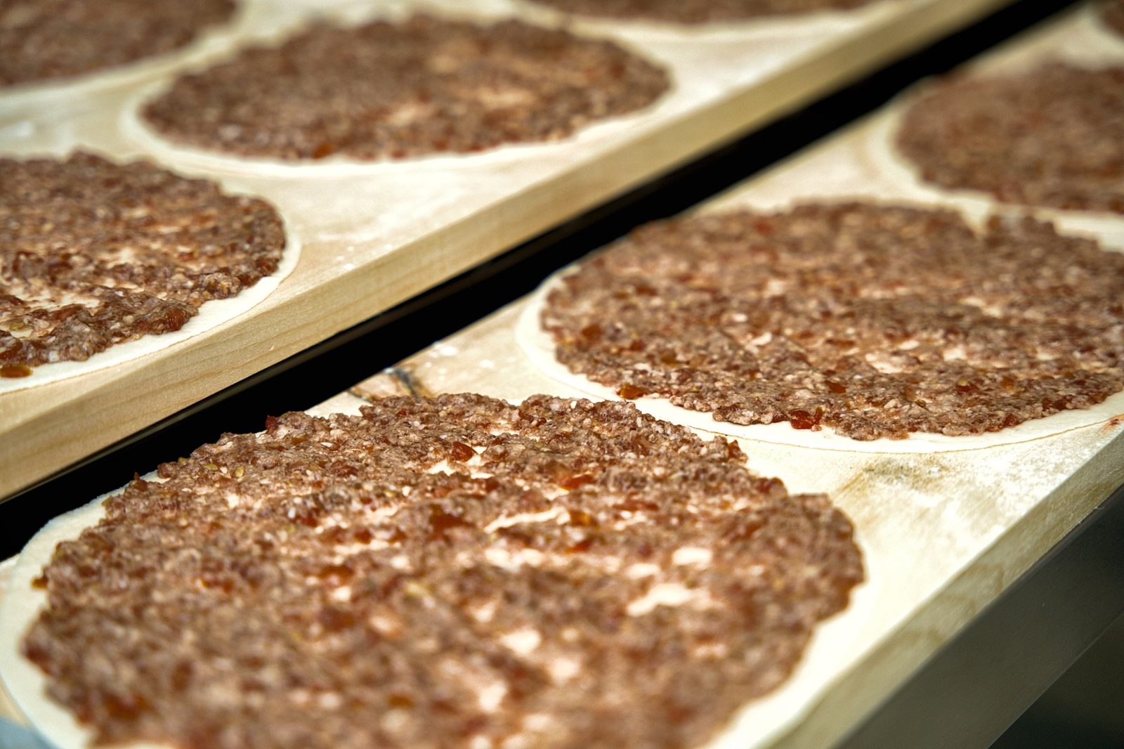 Raw lahm baajin laid out on a wooden bakery peel at Sahtein Bakery