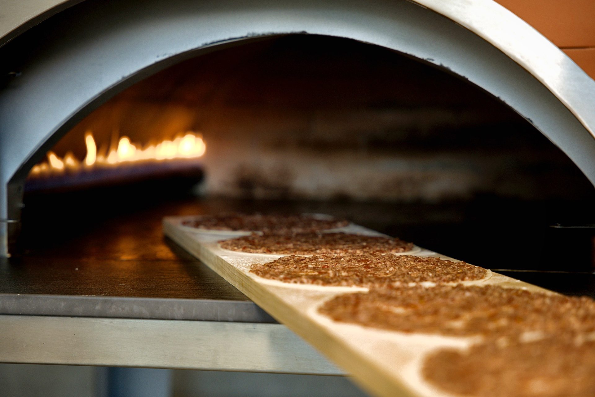 Freshly topped lahm baajin on a wooden peel heading into the wood-fired oven at Sahtein Bakery